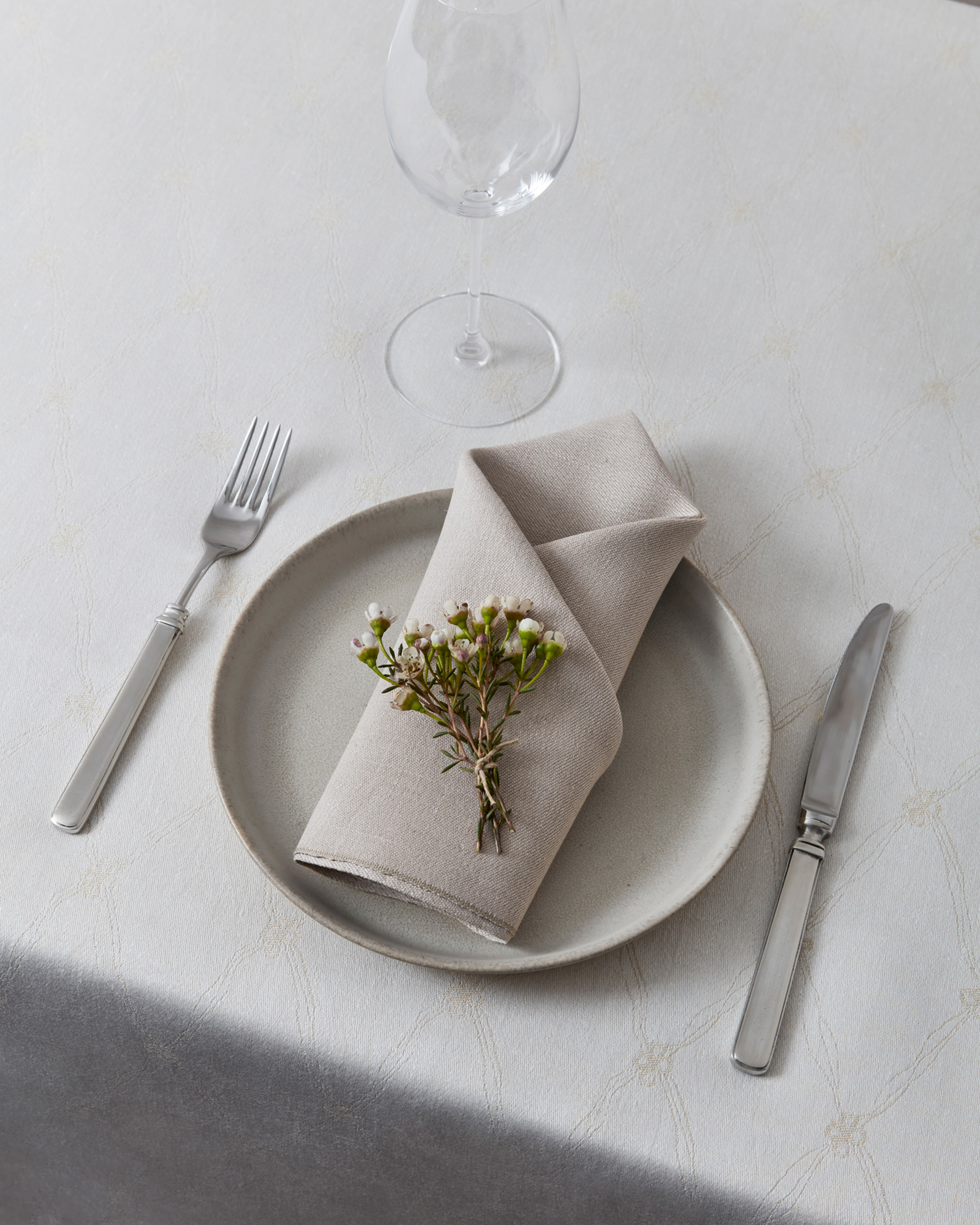 Iv Klöver canvas in the color champagne. Table setting with fork and knife as well as plate and napkin. Wine glass and a flower on the napkin. 