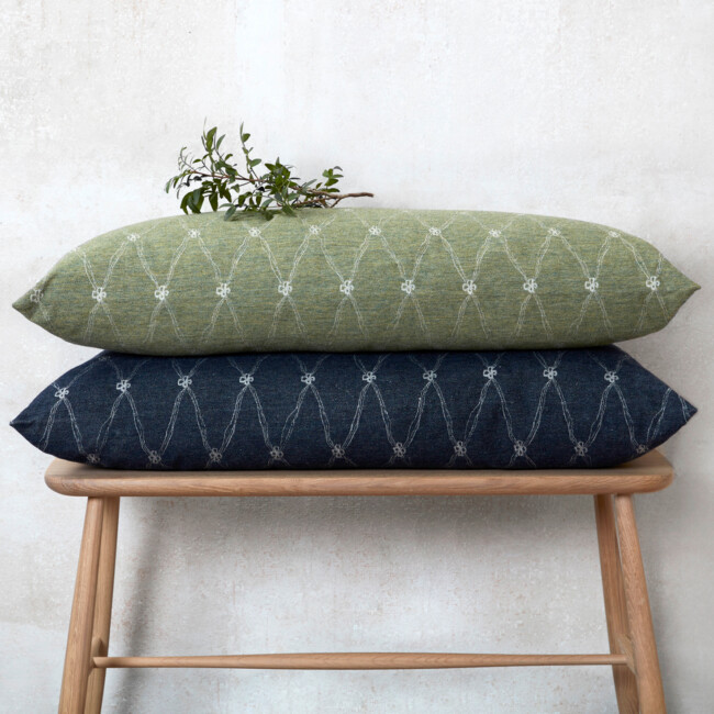 Oblong decorative pillows lying on top of each other, on a pallet. The colors dark blue and green with a clover pattern 