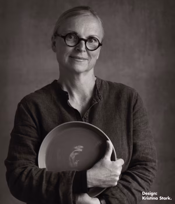 Formgivaren Krisitna Stark porträtt i svartvitt. Kristina står och håller i en tallrik som hon själv har designat.