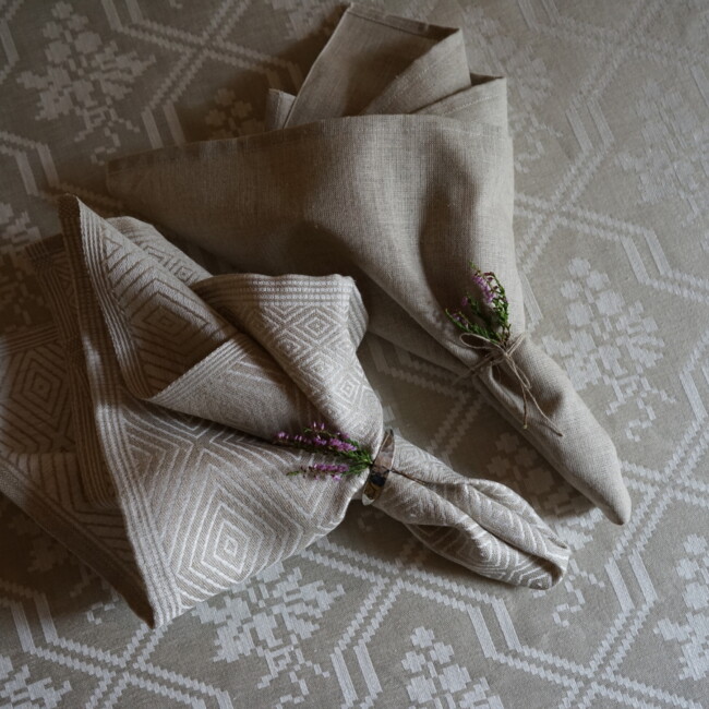 A Goose Eye and a Rustic napkin in a simple napkin fold, a lily adorns as a detail - klässbols linen weaving